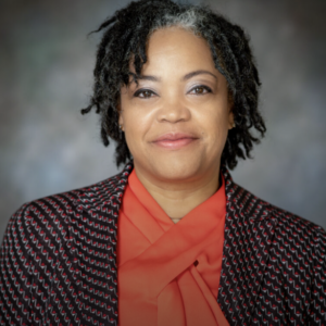 Woman with curly gray-streaked hair wearing an orange blouse and patterned blazer, portrait